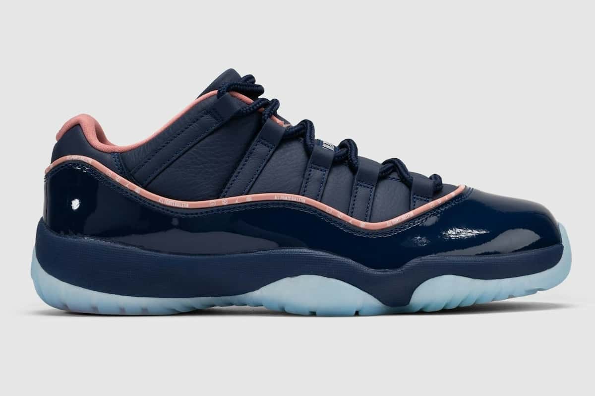 APB x Air Jordan 11 Low Made for Locals de perfil sobre fondo gris claro, con capellada de cuero azul marino, guardabarros de charol azul, vivo rosa con la leyenda All Points Bulletin y suela translúcida celeste