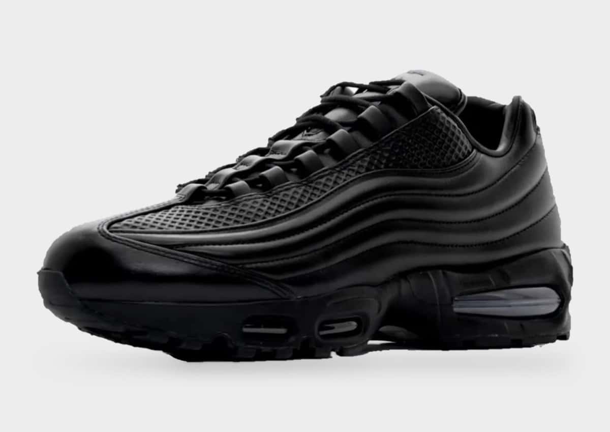 Nike Air Max 95 Lux de One Block Down de perfil sobre fondo gris claro, toda de cuero negro con las capas onduladas del lateral, cordones negros y la cámara Air azulada en el talón